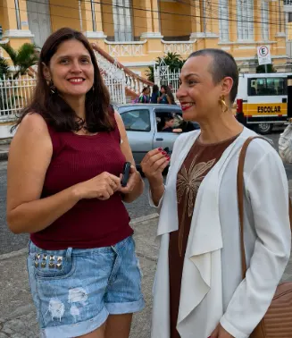 Renata Carvalho conversando com uma moradora na rua, em frente a uma escola.